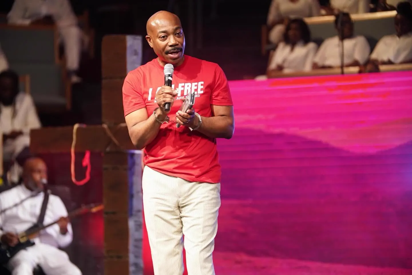 Member testifying on stage in an "I Am Free" shirt with broken chains