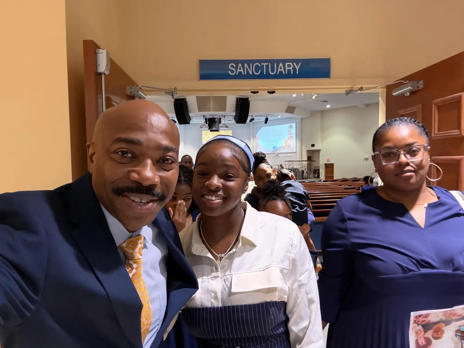 Pastor smiling with church members for a selfie near the sanctuary